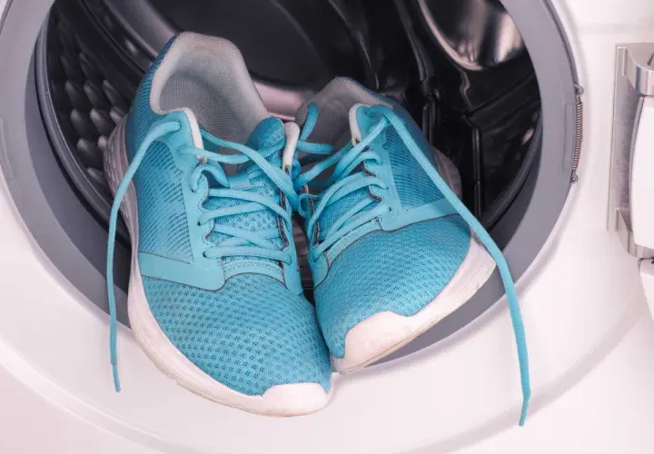 Paire de baskets bleues dans le tambour d'une machine à laver. Prêtes pour un cycle de nettoyage.