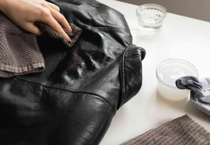 Maintenant, découvrez comment nettoyer une veste en simili cuir. Une main utilise un chiffon pour frotter la veste noire.