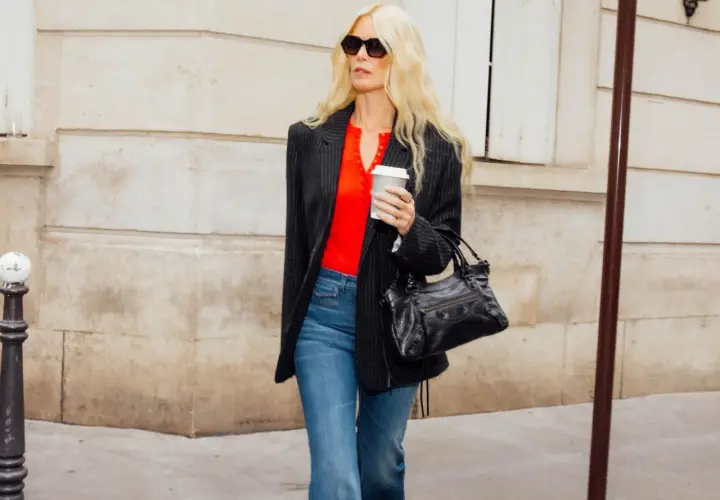 Femme blonde portant un jean évasé et un blazer rayé, avec un haut rouge vif et un sac à main noir.