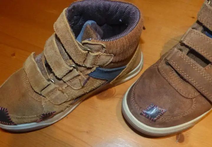Paire de bottines marron avec des patchs noirs et roses sur le bout de chaussure abîmé.