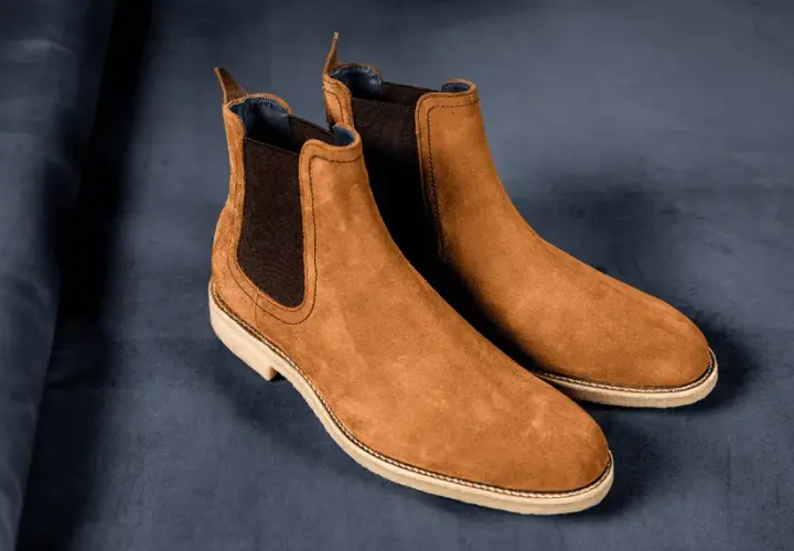 Paire de bottines Chelsea en daim marron, sur fond bleu nuit. La matière daim offre une texture douce et luxueuse.
