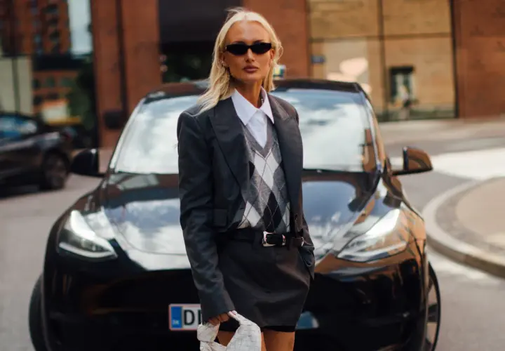 Une femme stylée devant une Tesla noire, portant un ensemble blazer et jupe gris. Un look parfait pour savoir quel blazer pour quelle morphologie.