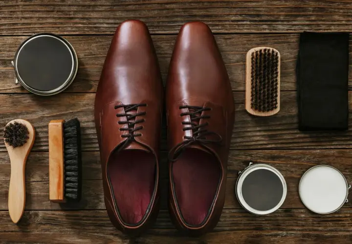 Paire de chaussures en cuir marron, prête pour un entretien. Brosse, cirage et chiffon pour protéger le cuir de la pluie.