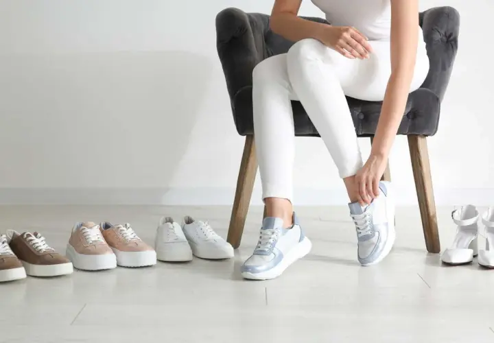 Choix de baskets pour une petite taille : une femme essaie des baskets bleues et blanches, entourée de plusieurs paires de chaussures.