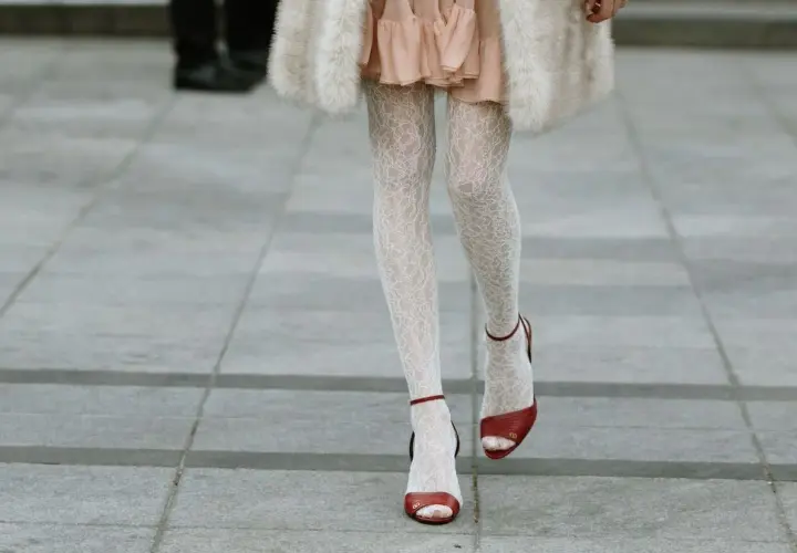 Jambes portant une chaussure ouverte avec collant blanc en dentelle, robe rose et manteau de fourrure.