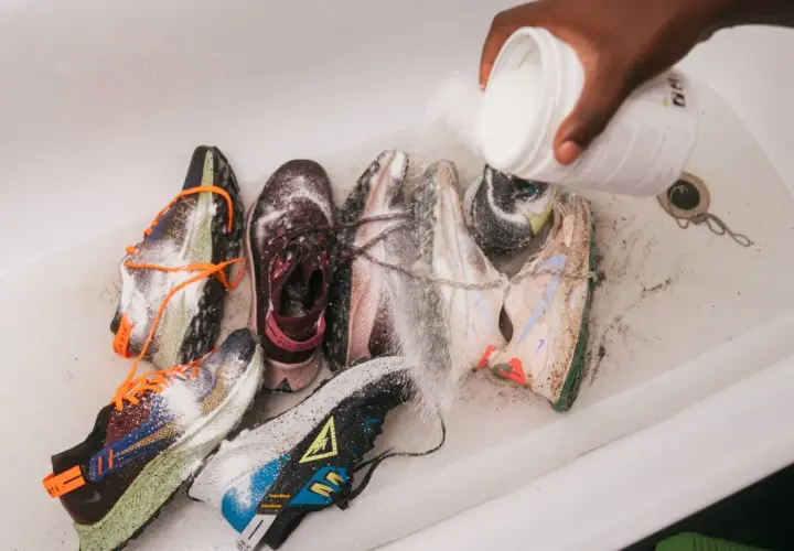 Une main verse une poudre blanche sur plusieurs paires de baskets dans une baignoire. C'est une étape clé pour savoir comment désinfecter des chaussures.