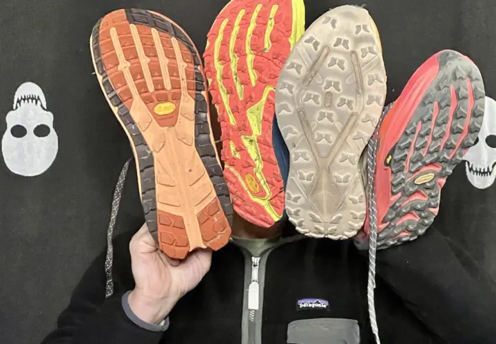 Qu'est-ce qu'une semelle Vibram ? Quatre semelles de chaussures de trail, dont une Vibram orange, montrent leur adhérence.