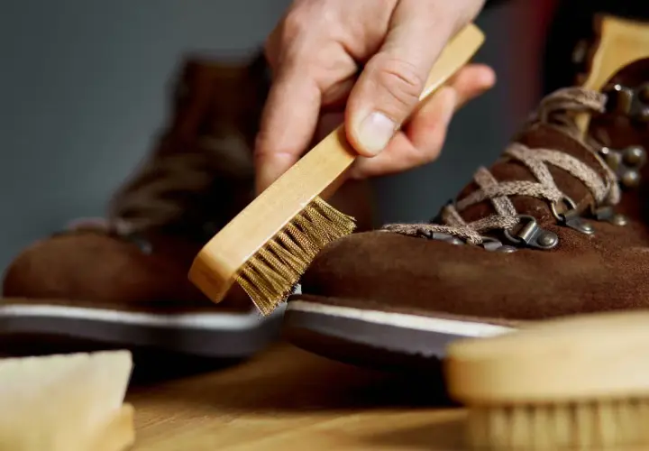 Maintenir vos chaussures en daim beige impeccables : une main utilise une brosse pour nettoyer le daim.
