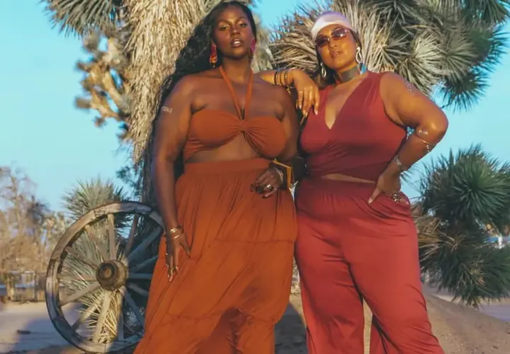 Deux femmes aux courbes généreuses posent dans le désert. L'une porte une robe longue orange, l'autre un ensemble pantalon et top rouge. Des tenues parfaites pour savoir comment s'habiller quand on a des grosses cuisses.