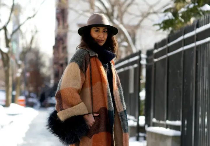 Une femme élégante avec un manteau coloré, un chapeau et un sac en fourrure, parfaite pour savoir comment s'habiller en hiver femme.