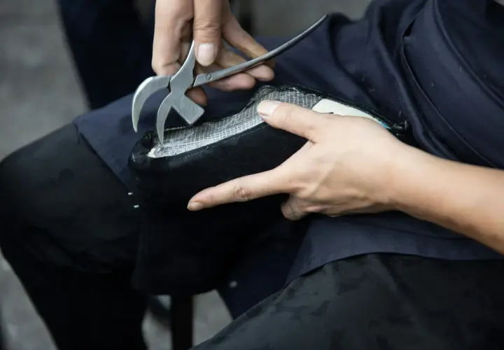 Un artisan utilise un outil pour travailler sur un objet en simili cuir noir. La question "peut on peindre du simili cuir" se pose face à cette métamorphose.