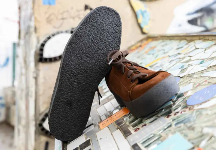 Une semelle crêpe noire repose contre une chaussure marron en daim. Le motif texturé de la semelle crêpe offre une adhérence robuste.