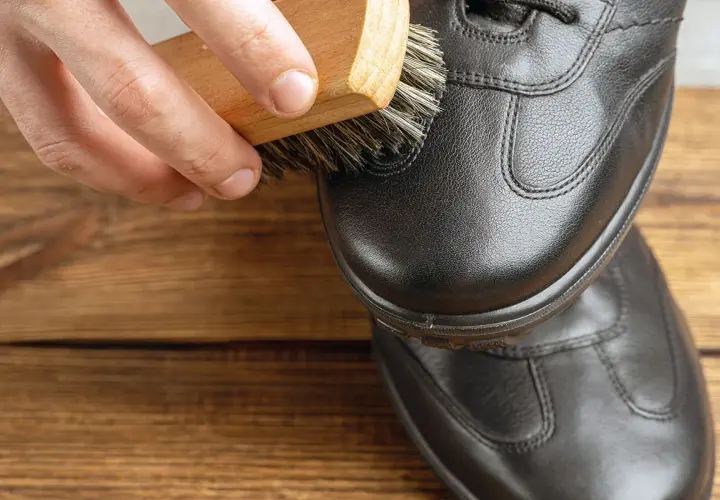 Maintenir le cuir en bon état : une brosse nettoie une chaussure noire pour réparer le cuir craquelé.