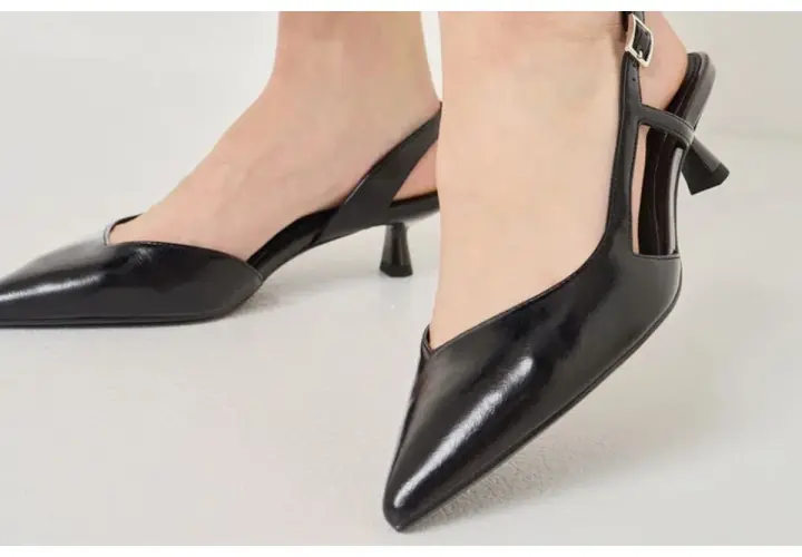 Pieds chaussés d'escarpins noirs vernis à talon carré et bride arrière. Idéal pour savoir comment porter des escarpins avec élégance.