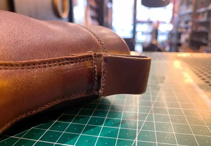 Gros plan sur une chaussure en cuir marron, montrant une déchirure à réparer. Le travail de réparation du cuir déchiré d'une chaussure est en cours.