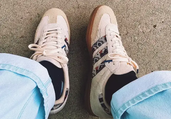 Un homme porte des sneakers Adidas beige avec des détails ethniques, un outfit décontracté parfait pour la belle saison.