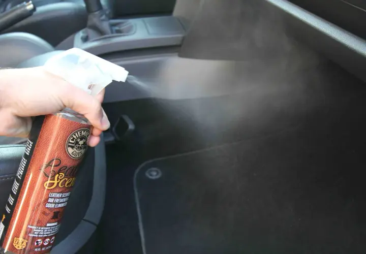Une main vaporise un produit pour voiture, diffusant une agréable odeur de cuir dans l'habitacle.