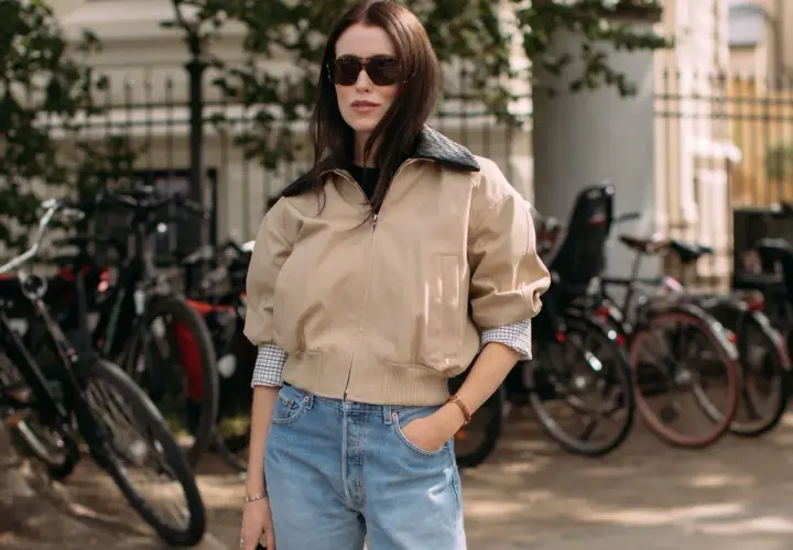 Une femme avec une morphologie H porte un jean bleu délavé et une veste beige.