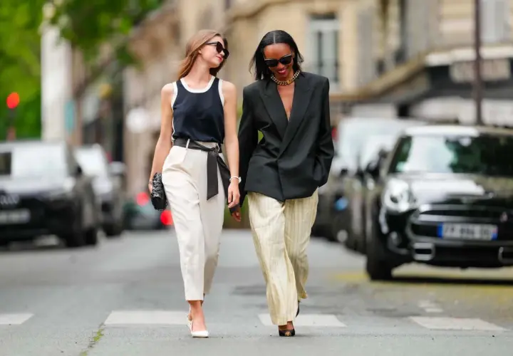 Deux femmes marchent dans la rue. L'une porte un pantalon blanc et un top noir, l'autre un blazer noir et un pantalon rayé. Idées pour comment s'habiller quand on est mince et petite.