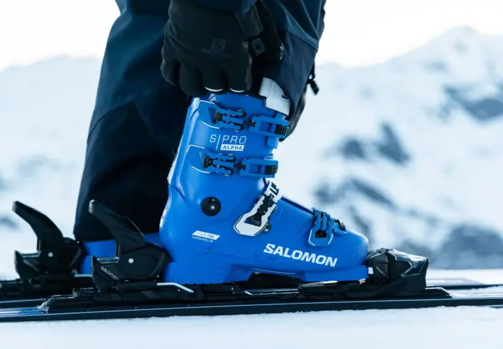 Une chaussure de ski Salomon bleue vif, prête pour la piste. Les boucles noires et blanches sont ajustées, la neige est au rendez-vous.