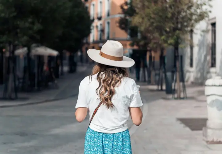 Une femme porte un chapeau et une robe fleurie, idéale pour savoir quelle couleur porter quand il fait chaud.