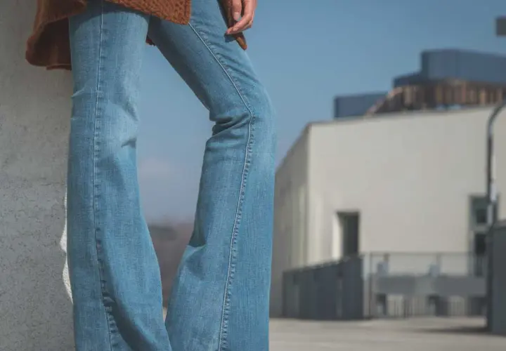 Un jean bootcut bleu clair, un pull marron et des baskets. Style décontracté pour une journée ensoleillée.