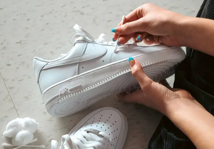 Main blanche, on nettoie une chaussure qui couine avec un coton-tige. Les ongles sont décorés de visages souriants.