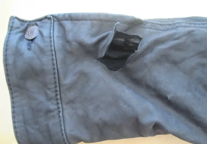 Gros accroc sur un vêtement en cuir, révélant la doublure intérieure. Le bouton sur le côté gauche est intact.