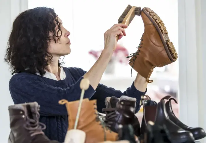 Une femme aux cheveux bouclés brosse une botte en cuir. Elle s'assure de la bonne fréquence de cirage de ses chaussures pour les garder en parfait état.