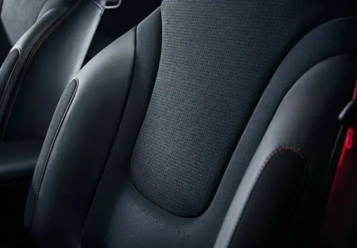 Sièges de voiture en cuir noir et matière alcantara, avec surpiqûres rouges contrastantes.