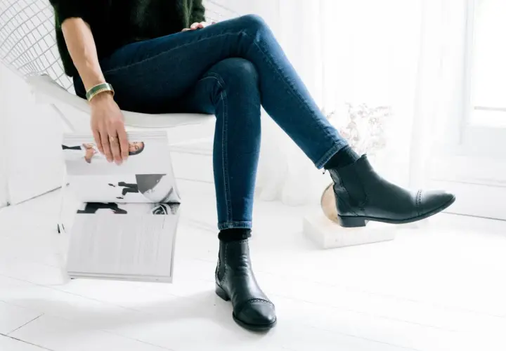 Une femme assise lit un magazine, portant un jean slim et des bottines Chelsea noires.