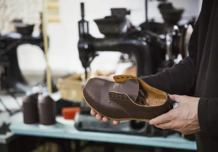 Un artisan examine une chaussure de ville en cuir marron, signe qu'il est temps de penser à quand changer ses chaussures de ville.