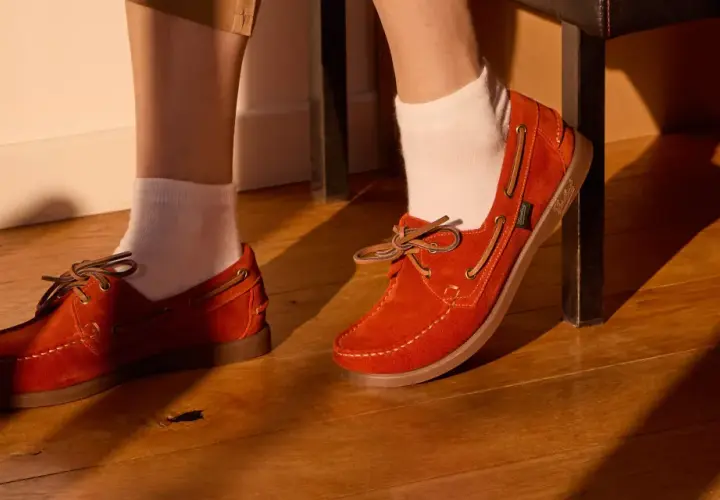 Chaussure bateau femme look : des mocassins en daim orange vif avec lacets en cuir, portés avec des chaussettes blanches sur un parquet en bois.