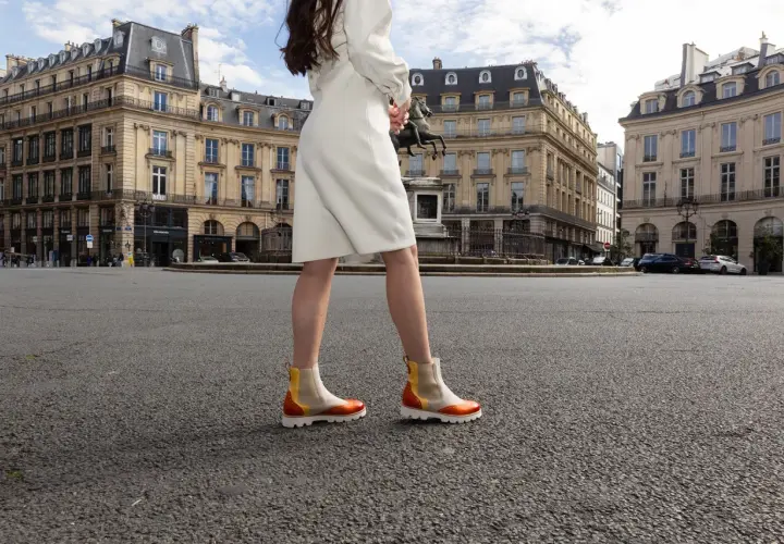 Une femme porte des bottines colorées en plein été, marchant sur une place parisienne.