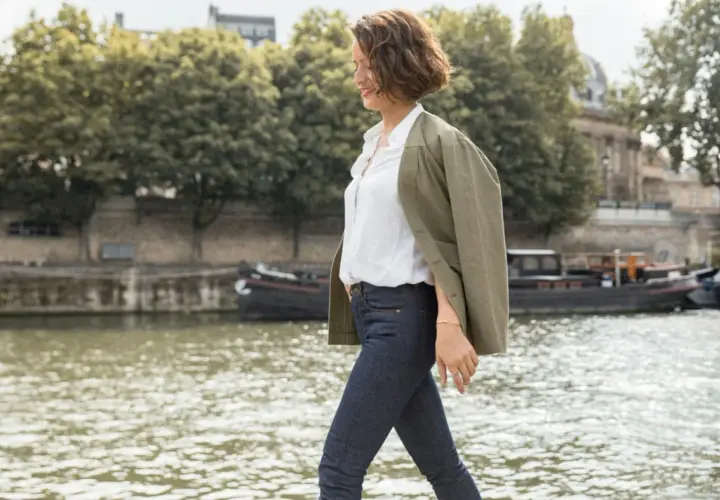 Une femme élégante à Paris, parfaite pour savoir comment s'habiller quand il fait 10 degrés femme : jean, chemise blanche et veste kaki.