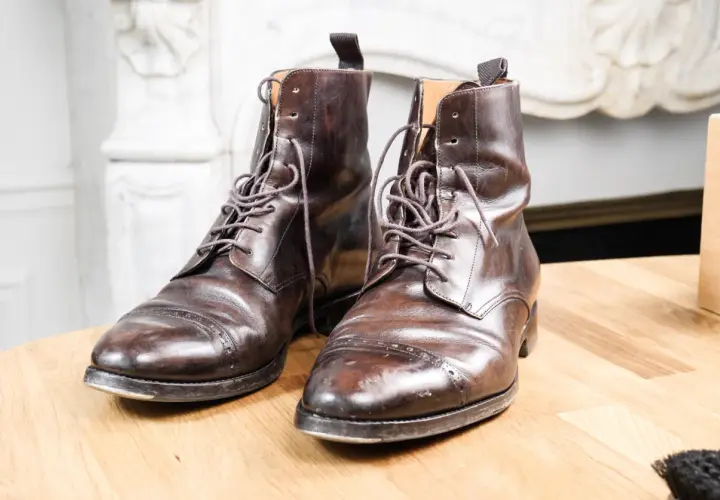 Paire de bottines en cuir griffé marron foncé, lacets serrés, posées sur une table en bois.
