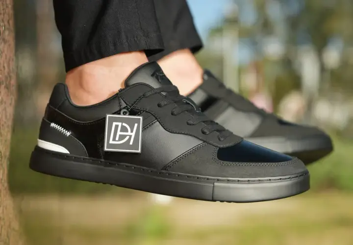 Baskets noires stylées, avec un jean qui détient sur la chaussure. Logo DH sur une étiquette.