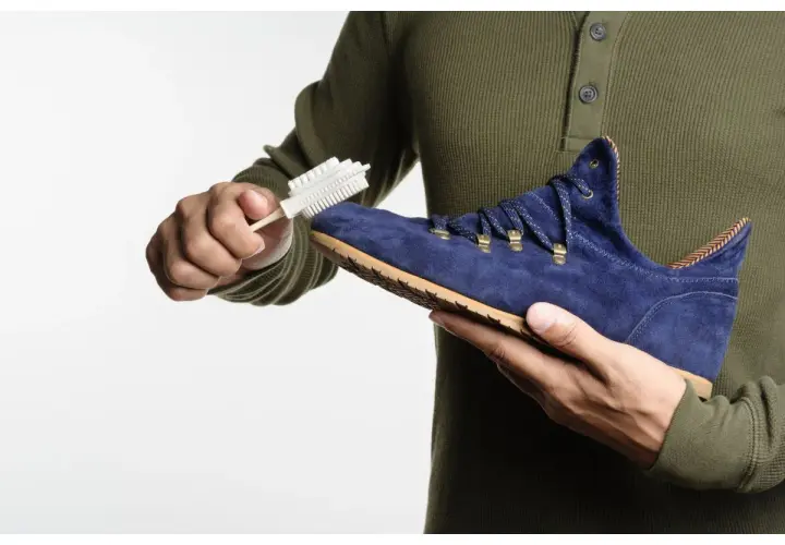 Maintenir le cuir suédé en bon état : une main brosse une chaussure bleue avec une brosse spéciale.