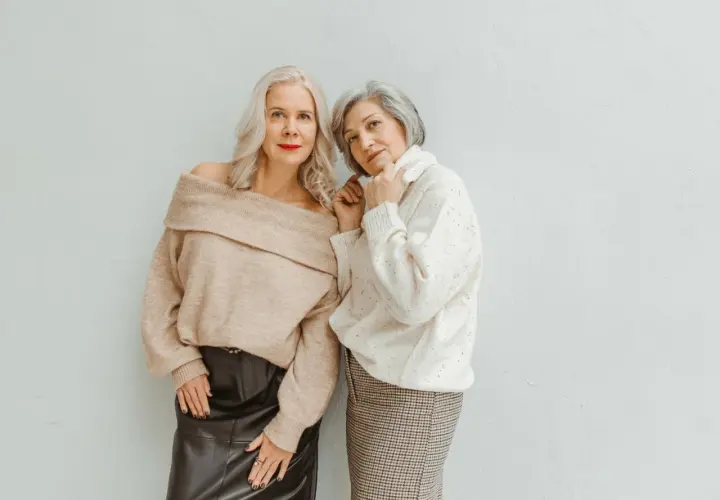 Deux femmes élégantes, l'une en pull beige dénudant ses épaules et jupe en cuir, l'autre en pull blanc et jupe à carreaux, prouvent qu'il n'y a pas d'erreurs de style qui vieillissent.