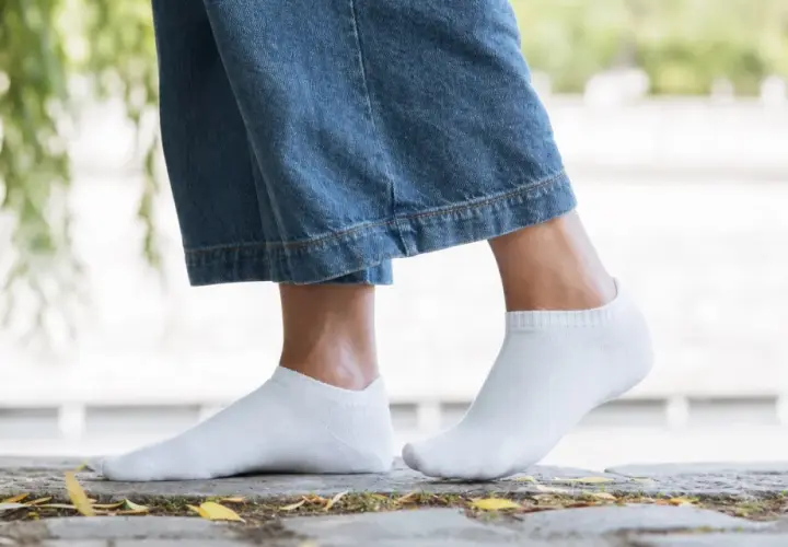 Pieds féminins en chaussettes blanches discrètes, idéales avec des baskets blanches pour un look casual.