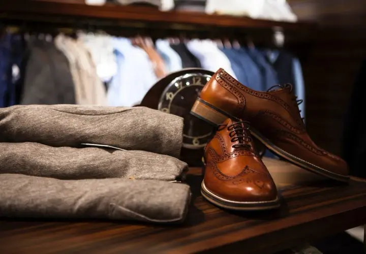 Chaussures en cuir marron élégantes, prêtes à être assouplies. Un pull plié et un manteau sont visibles en arrière-plan.