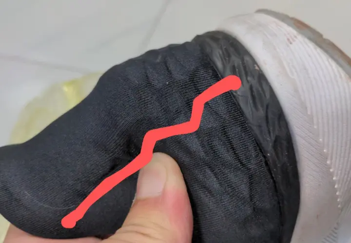Un pouce appuie sur le contrefort d'une chaussure noire, révélant une fissure.