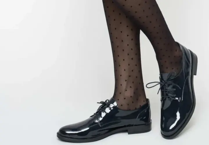 Pieds chaussés de derbies vernies et collants à pois. Idéal pour savoir comment porter des derbies femme avec élégance.