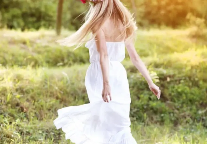 Une jeune femme aux cheveux blonds, portant une couronne de fleurs et une robe blanche légère, incarne l'esprit du printemps. Elle danse dans un champ verdoyant, une vision parfaite pour savoir comment s'habiller au printemps.