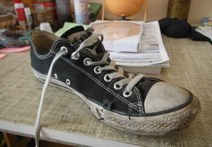 Une chaussure Converse noire usée, avec la semelle qui se décolle, témoigne de nombreuses aventures.