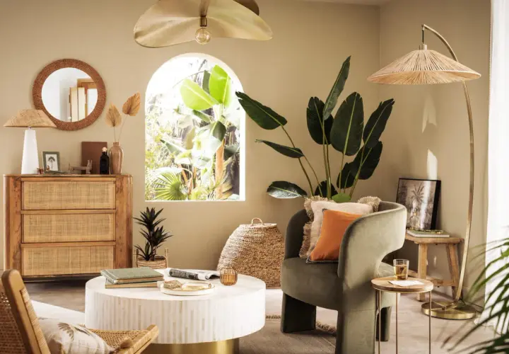 Salon bohème avec meubles en rotin et touches dorées. Le vert du fauteuil et l'orange du coussin s'accordent bien avec le doré.