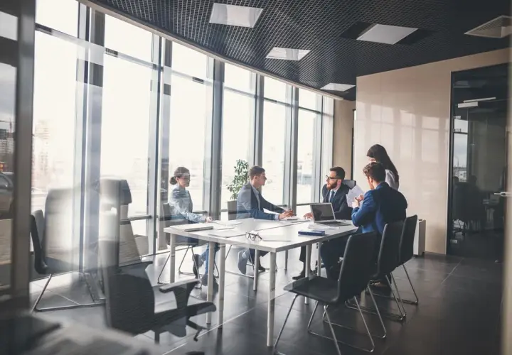 Des employés en tenue pour réunion travail discutent autour d'une table dans une salle de conférence lumineuse avec vue sur la ville.