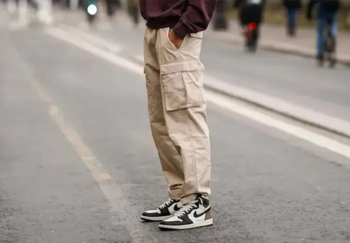 Un homme porte un pantalon cargo beige et une chaussure de sport iconique, prêt pour une journée en ville.