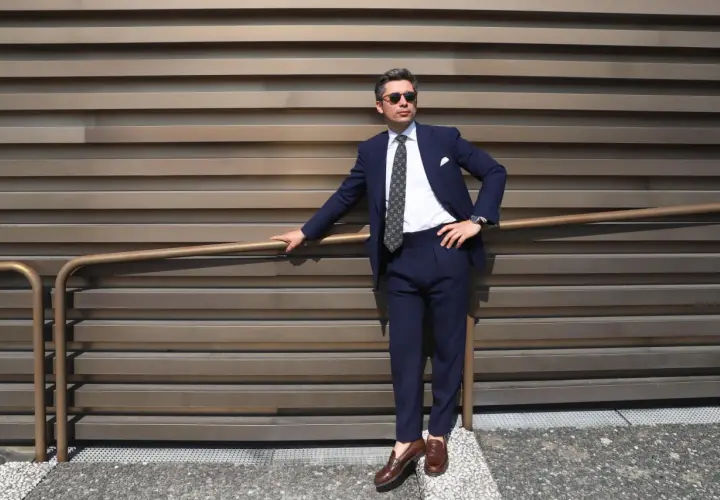 Un homme élégant porte un costume bleu marine, une chemise blanche et une cravate à motifs. Ses chaussures marron complètent parfaitement sa tenue.