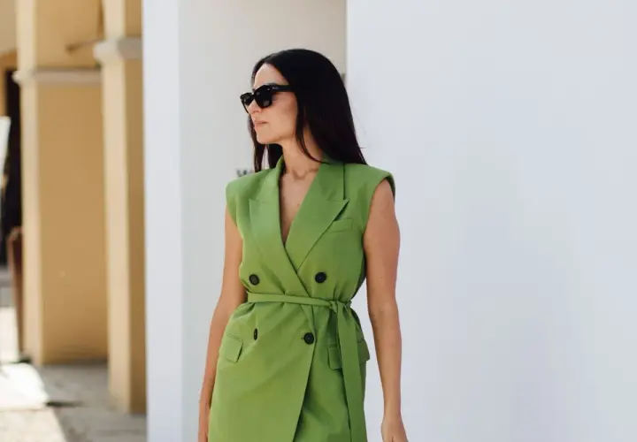 Une femme en robe blazer verte, lunettes de soleil, incarne pourquoi bien s'habiller au travail : confiance et professionnalisme.